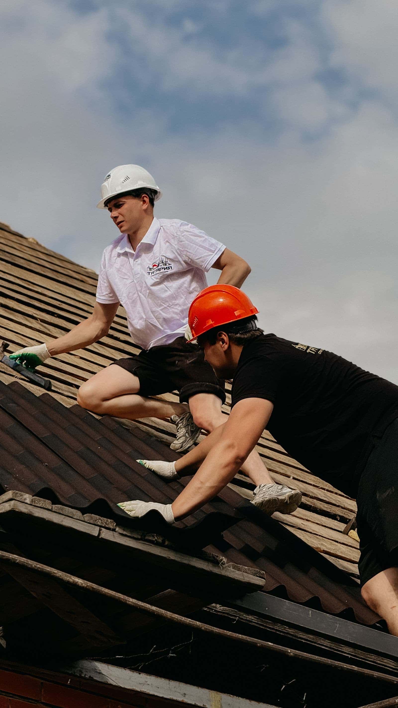 Roofers in safety gear working on a damaged roof